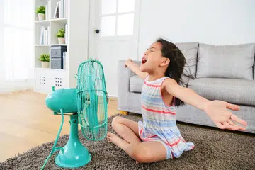 Happy female child kid opening arms and enjoying cool wind from an electric fan in the living room. Image from Freepik