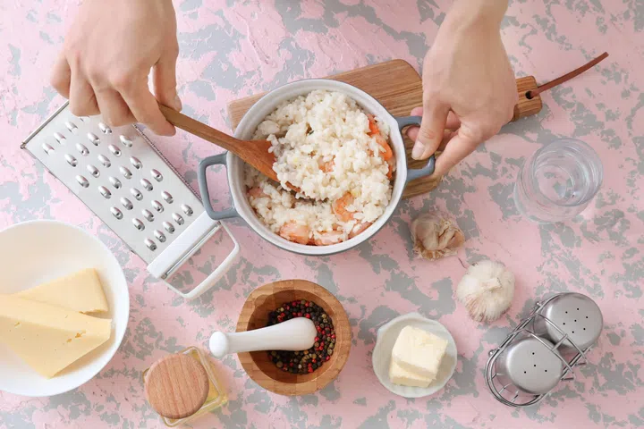 Woman cooking tasty risotto at table