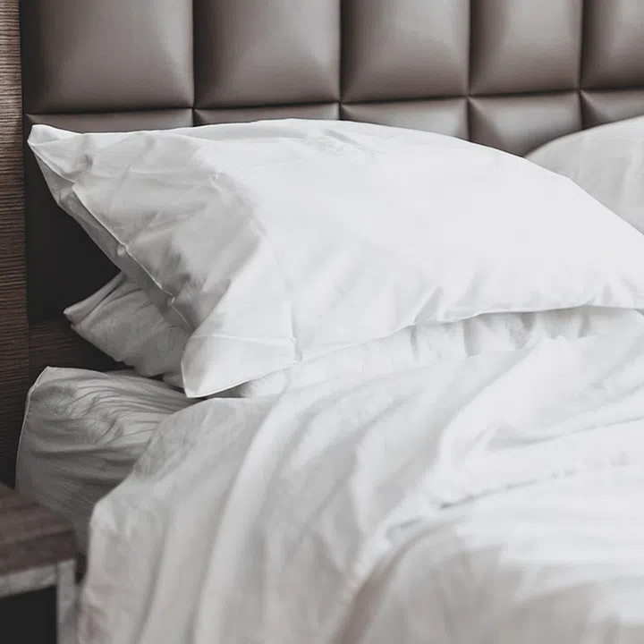 A stack of white pillows and white duvet on a bed with a quilted headboard.