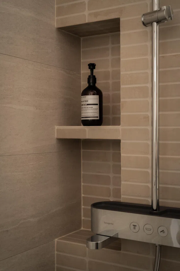 A recessed shower niche and warm, stone-look tiles create a calm, tactile backdrop.