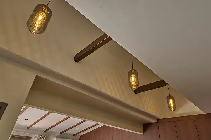 Previously concealed beams are exposed to introduce rhythm and texture overhead, paired with warm pendant lighting.