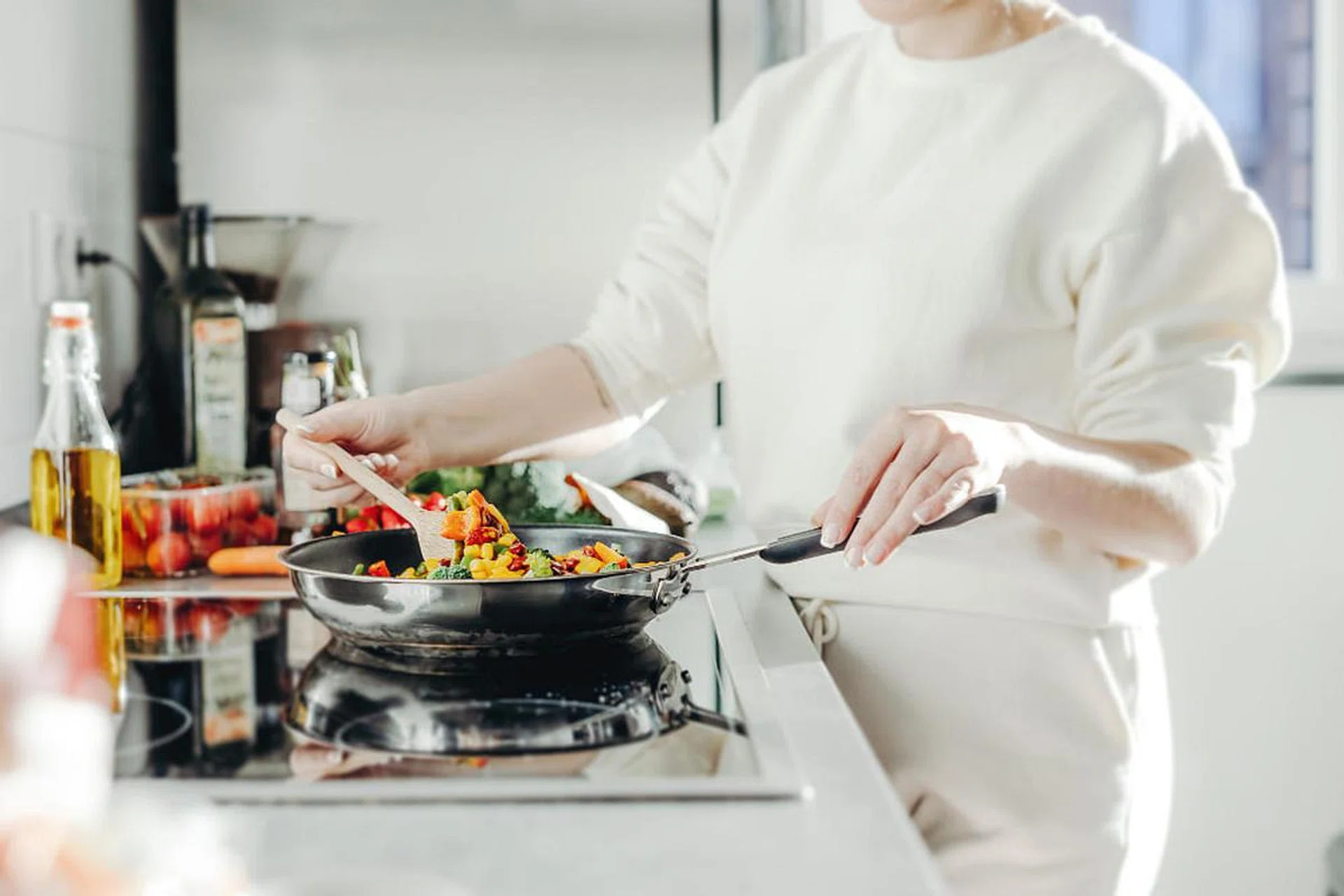 Woman cooking vegetables in a pan on an induction stove.