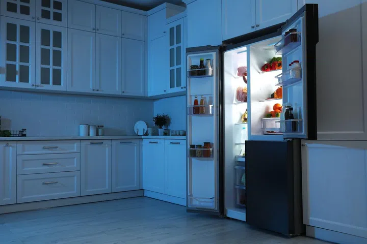 Open double door fridge with lights on in a dark kitchen
