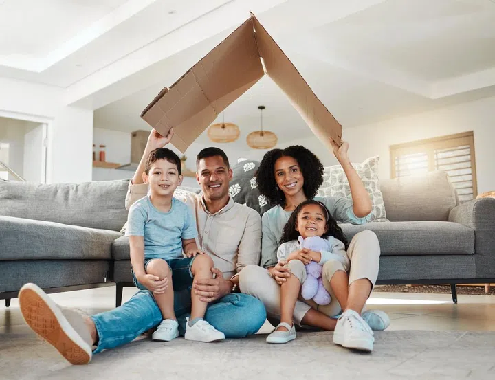 Cardboard roof, portrait and a family in a home for security, safety and shelter as a family. Happy, house and a mother, father and children with refuge in a living room for insurance together. Photo 123RF