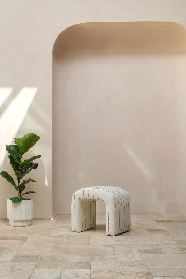 A white curved stool set against a cream wall with an arch and indoor house plant. Image by Kuky Home Collection, Natelee Cocks.