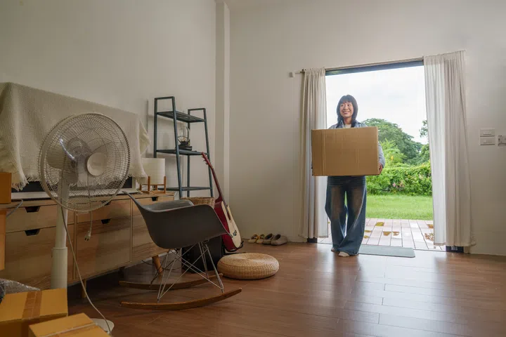 Smiling woman carrying cardboard box through doorway on moving day.