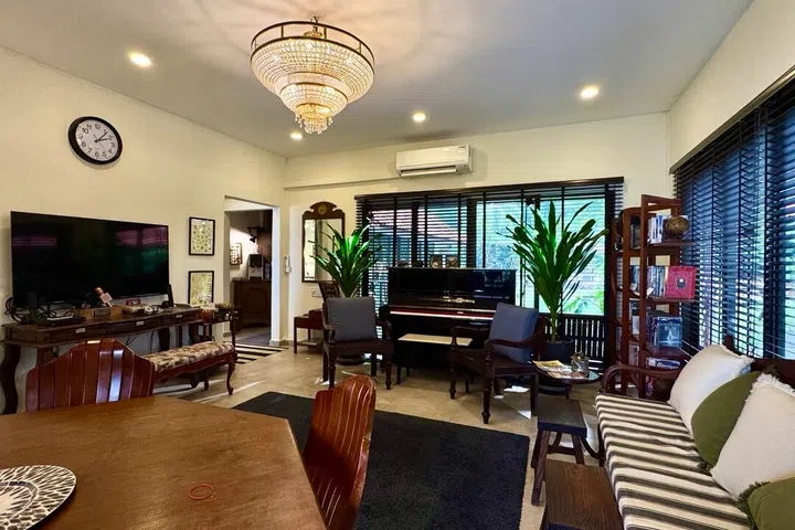 Large windows flood the main living space with light, highlighting the crystal chandelier, piano, and dark timber furnishings that define the home’s vintage charm.