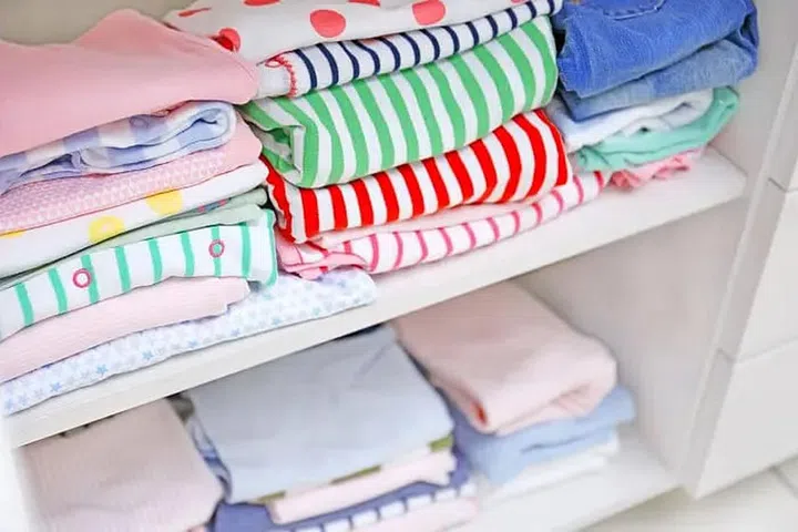Stacks of neatly folded baby clothes, napkins, towels in white shelves. Photo 123RF