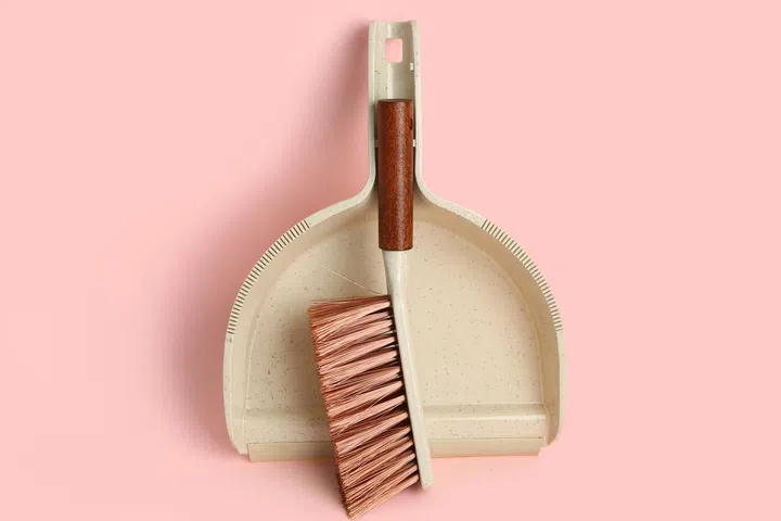 Dustpan and cleaning brush on pink background