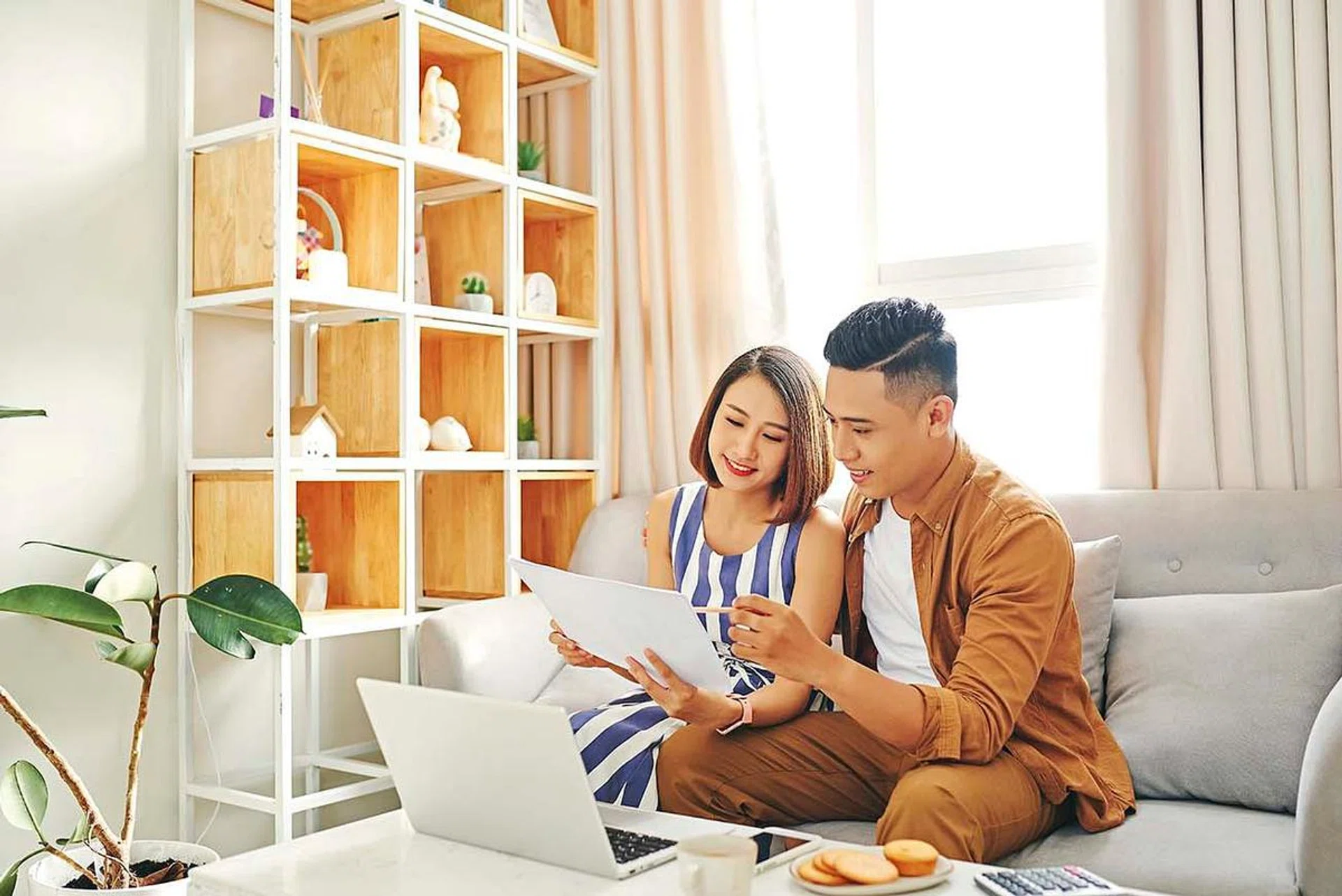 Portrait of beautiful young Asian couple using laptop on the sofa at home.