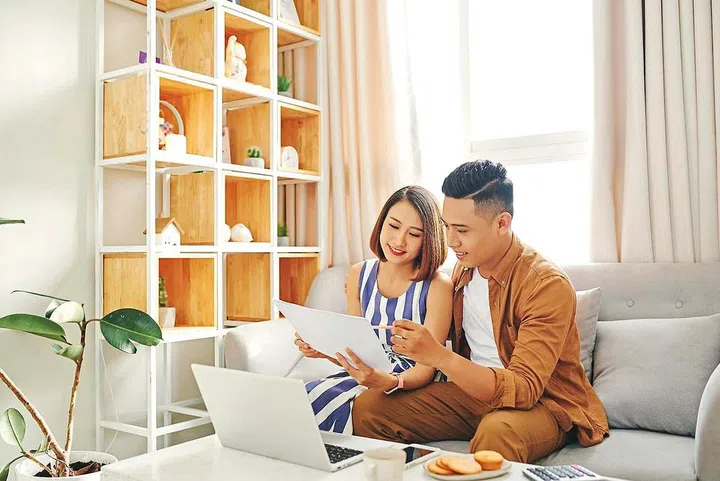Portrait of beautiful young Asian couple using laptop on the sofa at home.