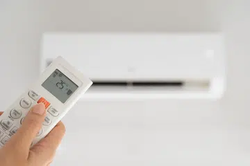 Woman hand holding remote controller directed on the air conditioner inside the room and set at ambient temperature, 25 degrees Celsius.