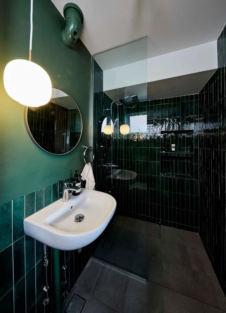 The rich emerald hue of the master bathroom tiles shines against the matte finish of the light green on the walls and pipe.