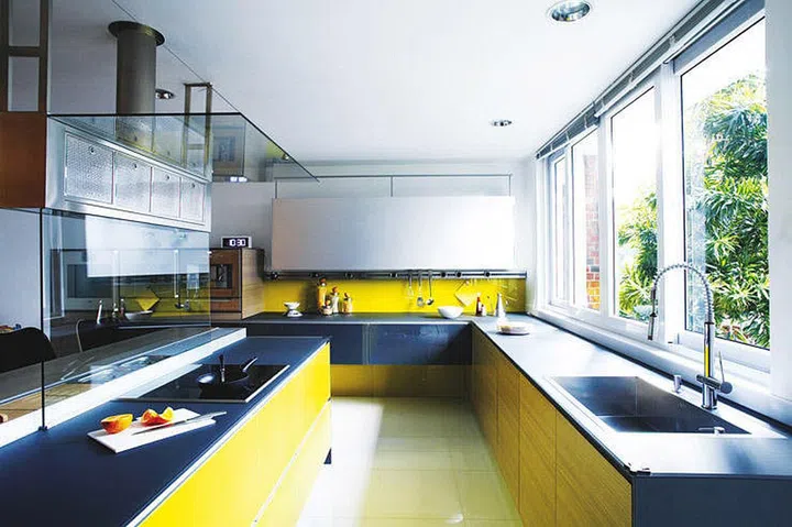 Yellow and blue kitchen with a swanky vibe by separating the diners from the chef with a sleek glass divider on the shared kitchen island.