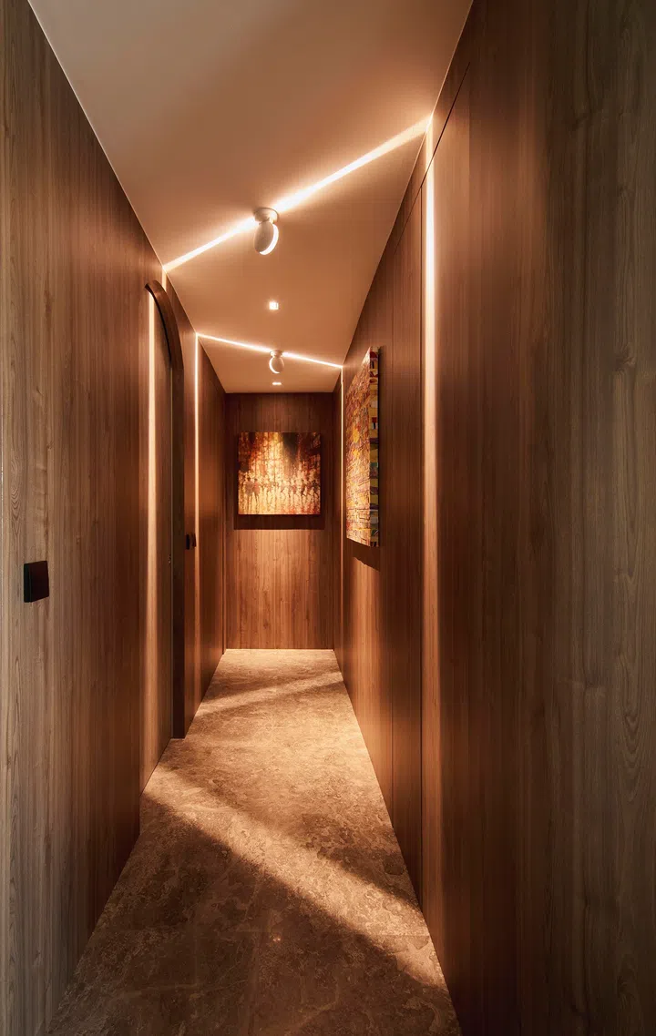 A gently lit passageway wrapped in full-height wood cladding, where hidden doors and seamless storage maintain spatial flow and quiet elegance.