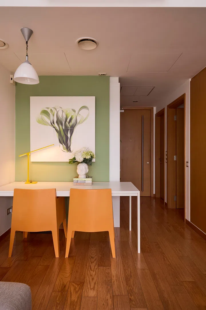 The dining area carries through the home’s palette, where a simple white table and orange chairs sit against a soft green wall.