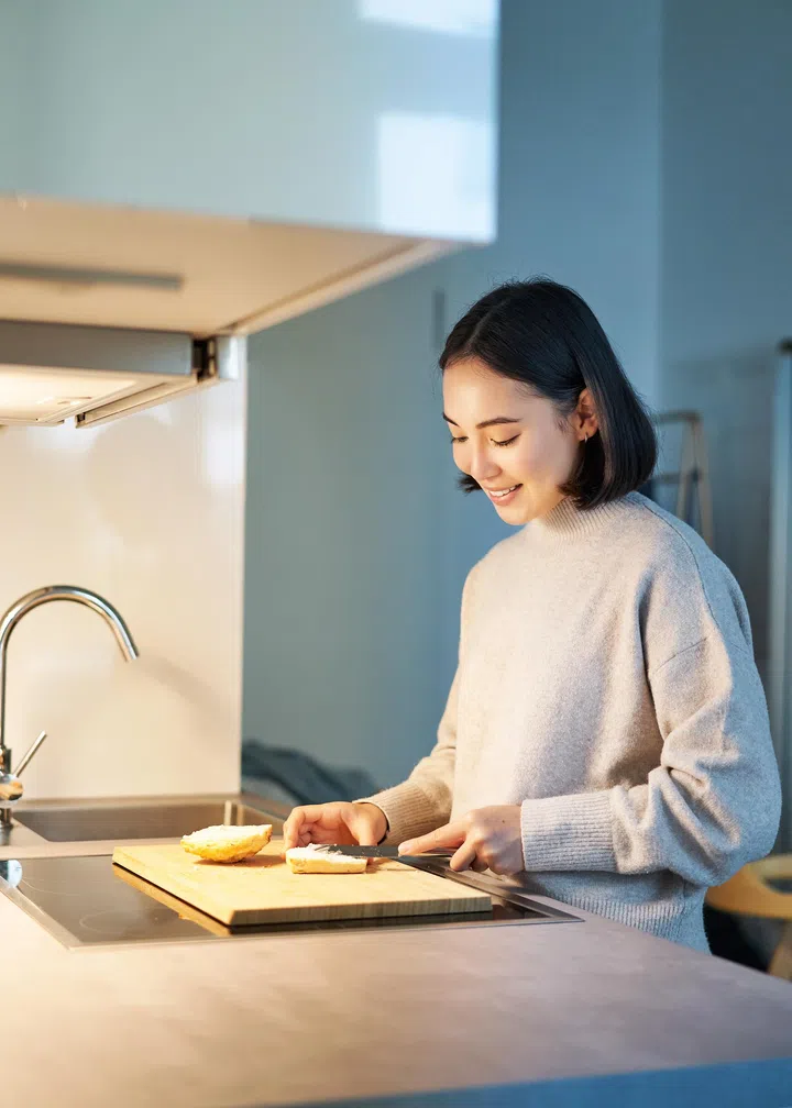 Vertical shot of young asian woman cooking dinner, making herself sandwitch, smiling while standing on the kitchen.