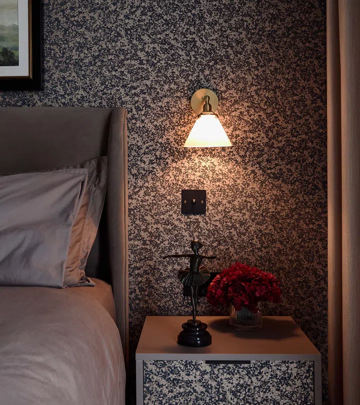 A dark, moody bedside setup reflects his style, with a patterned wall and unique trinkets adding character.