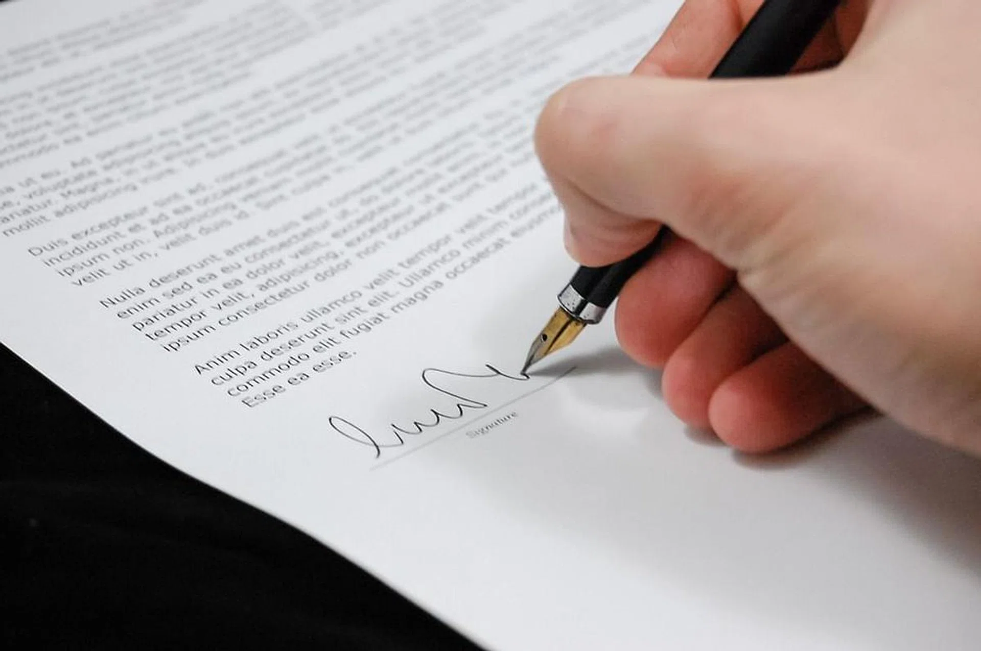 Hand holding black pen signing a contract. Photo from Pxabay