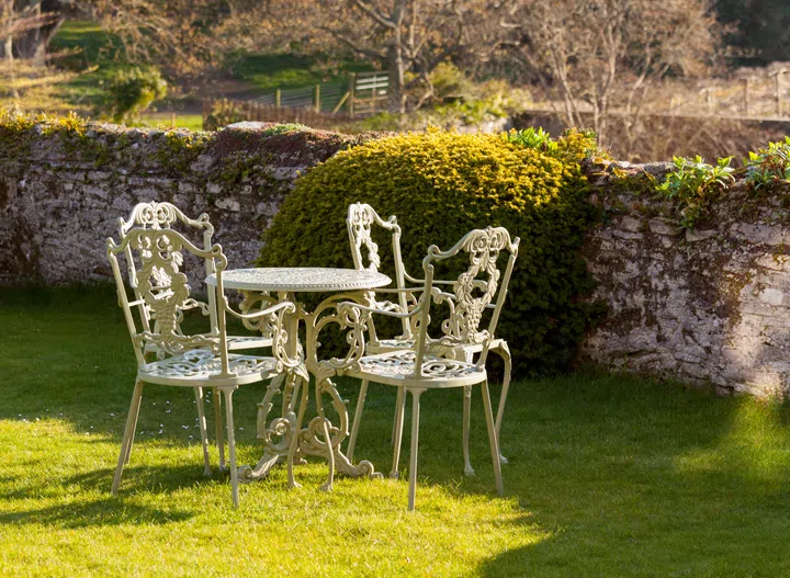 Cast iron garden table and chairs on lawn by stone wall
