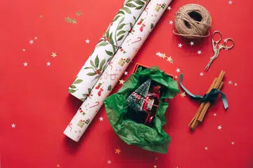 Christmas wrapping paper, rolls of paper, scissors, rope and christmas tree on red background. Image from 123RF