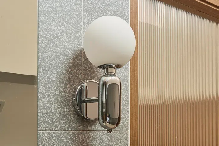 A globe wall light introduces a subtle contrast of form and finish against the textured wall surface.
