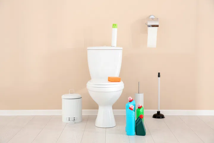 Ceramic toilet bowl, bottles of detergent and cleaning supplies in modern bathroom