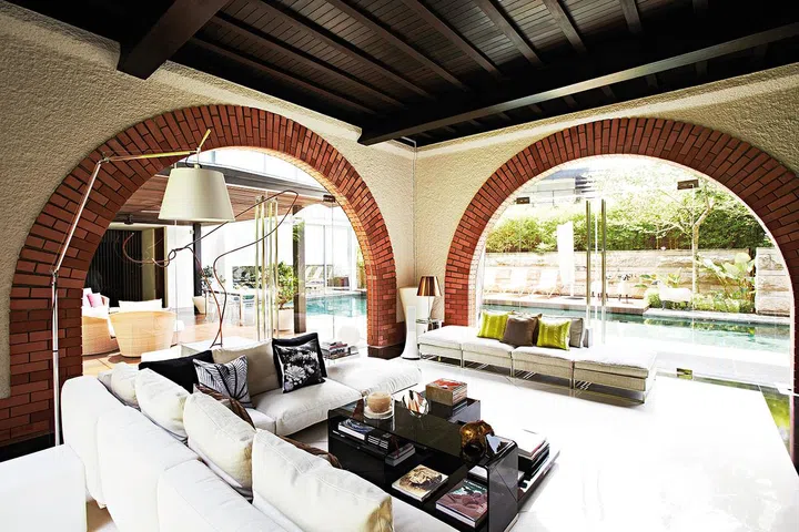 The stunning brick arches that surround the living area, already sealed up with glass doors, let the family enjoy views of the pool and greenery without being bothered by the weather outside. Interior design by Mofasis