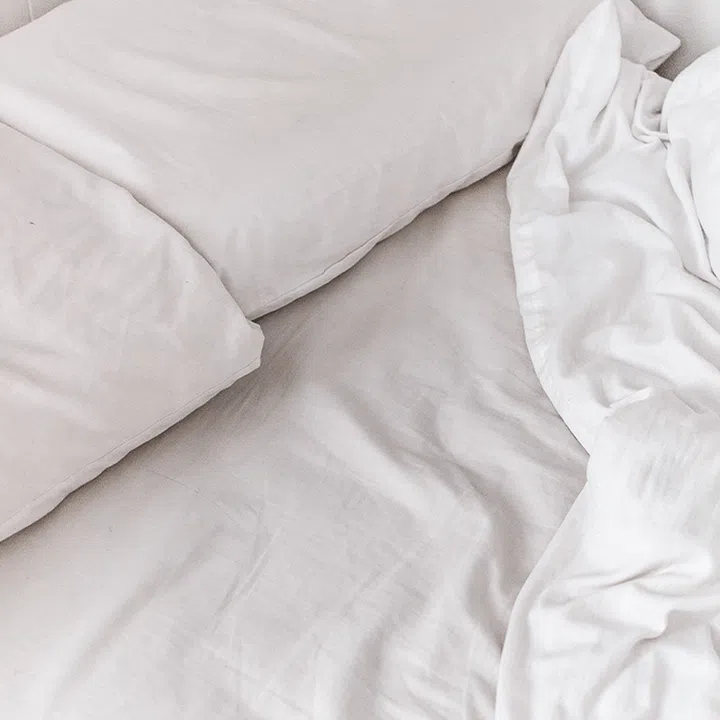 Close up of two pillows and duvet on a bed, all in white linens.