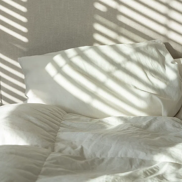 Shadows from window nearby cast on a stack of white pillows on duvet on a bed.