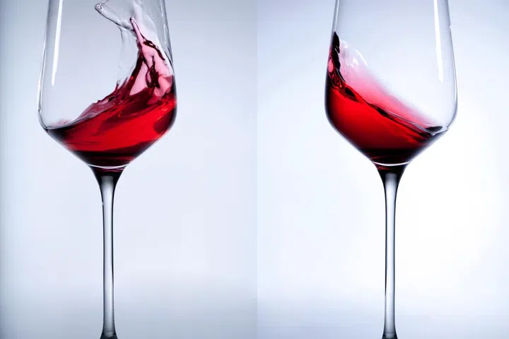 Red wine splashing in the elegant wine glass on gray background.