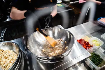 In the heart of a bustling kitchen, a chef expertly stirs sizzling ingredients in a wok.