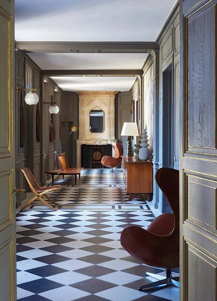 The original stone fireplace from the 17th century was created by Pierre de Bourgogne. On the right, a buffet by George Nakashima; sculptural lamp by Philippe Anthonioz; Egg chairs by Arne Jacobsen. On the left, a pair of AX chairs in laminated mahogany and leather by Peter Hvidt and wall light fixtures by Ignazio Gardella.