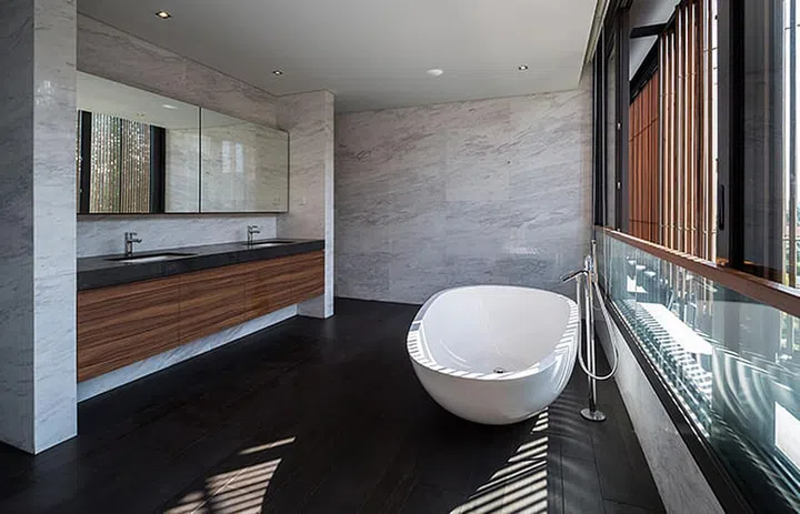 The bathroom is simple yet elegant, with marble walls and dark wood accents, punctuated by a free-standing bathtub.