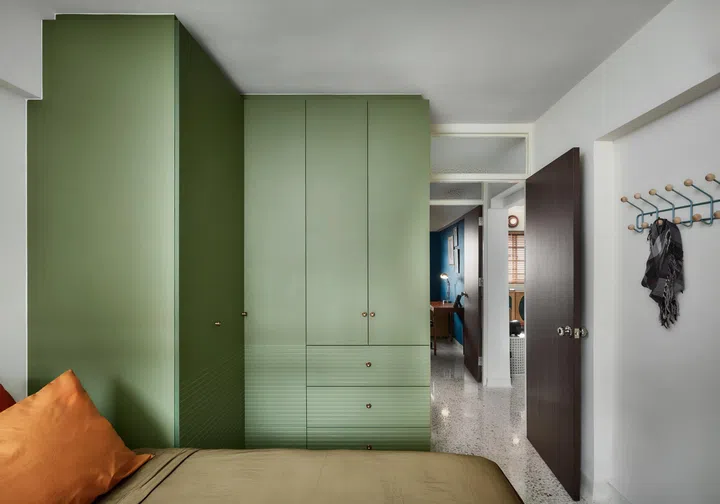 Green-toned wardrobes with subtle groove detailing anchor the bedroom, where small crafted touches soften the built-in elements.