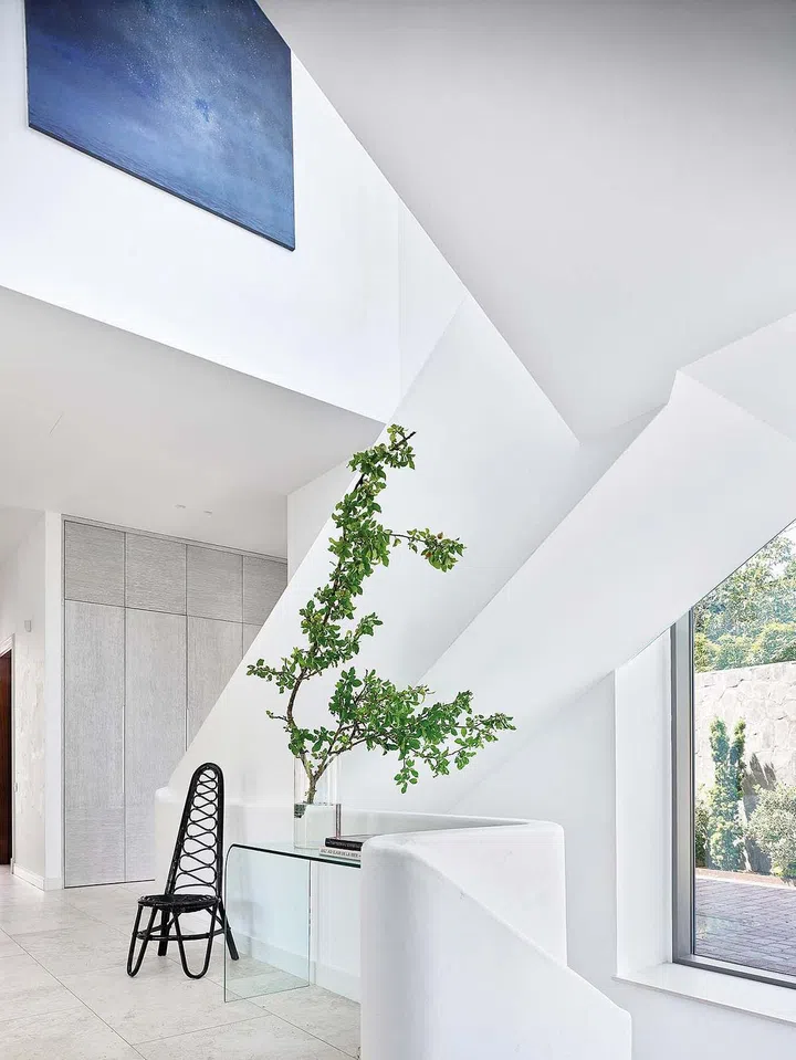 Dark-stained high-back Dirk Van Sliedregt vintage rattan chair creates a contrast with the gentle curves of the staircase and the glass console.