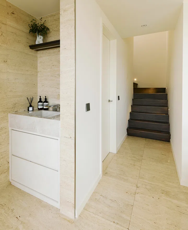 A view from the dry kitchen highlights the flow between the living spaces, with the stone vanity and sculptural staircase creating an understated focal point.