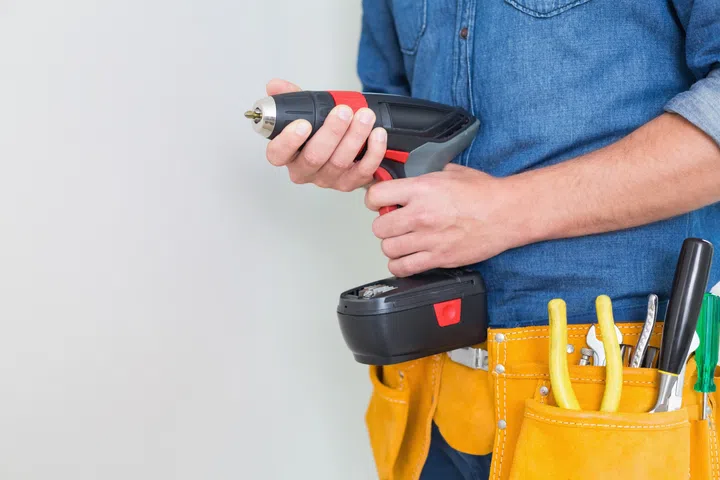 Close up mid section of a handyman with drill and toolbelt by the wall.