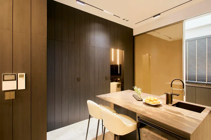 A concealed door within the dark carpentry discreetly reveals a powder room, keeping the kitchen façade clean and uninterrupted when closed.