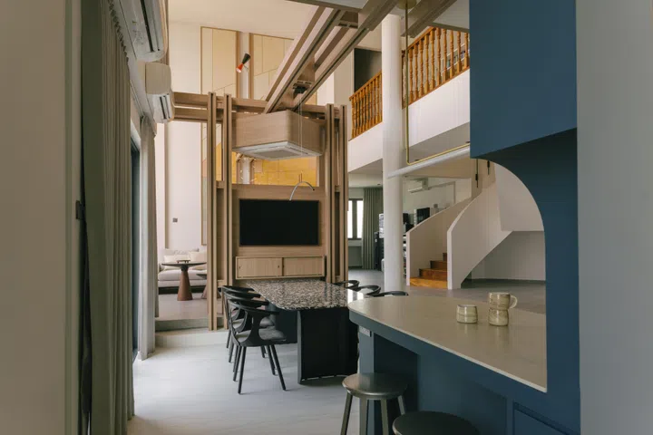 The dining area sits beneath the timber axis, where a suspended cassette air-conditioning unit anchors both airflow and gathering.
