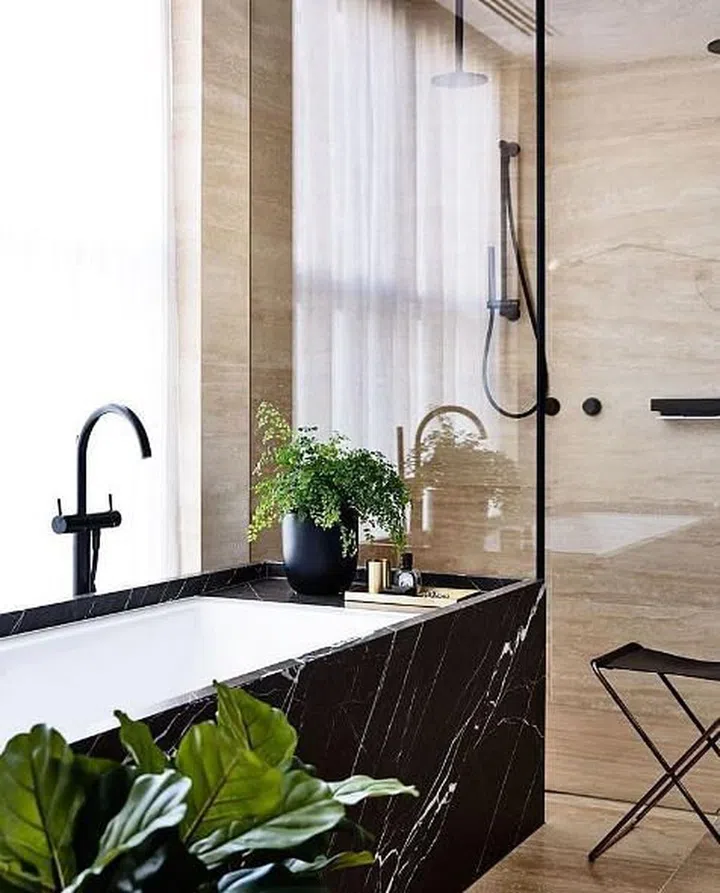 Black and white bathroom sink cabinet set against a clear glass panel with black frames. Bathroom laid in neutral cream marble wall and floor tiles.
