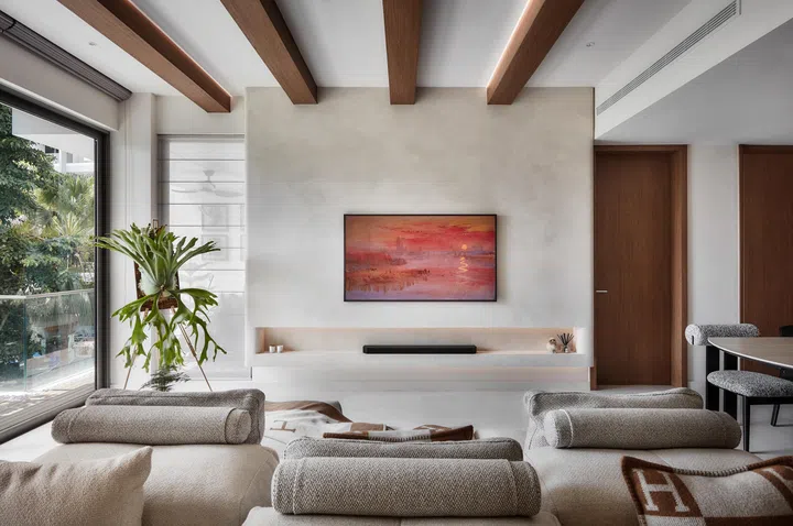 Warm wood beams and a textured limewash wall frame the living area, where the designers introduced hidden LED lighting to create a soft, sunset-like glow.