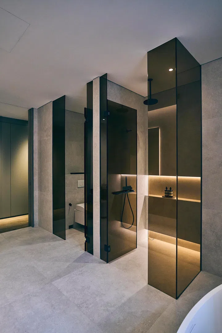  Tinted glass partitions add privacy while large-format tiles and black fixtures streamline the bathroom into a calm, modern retreat.
