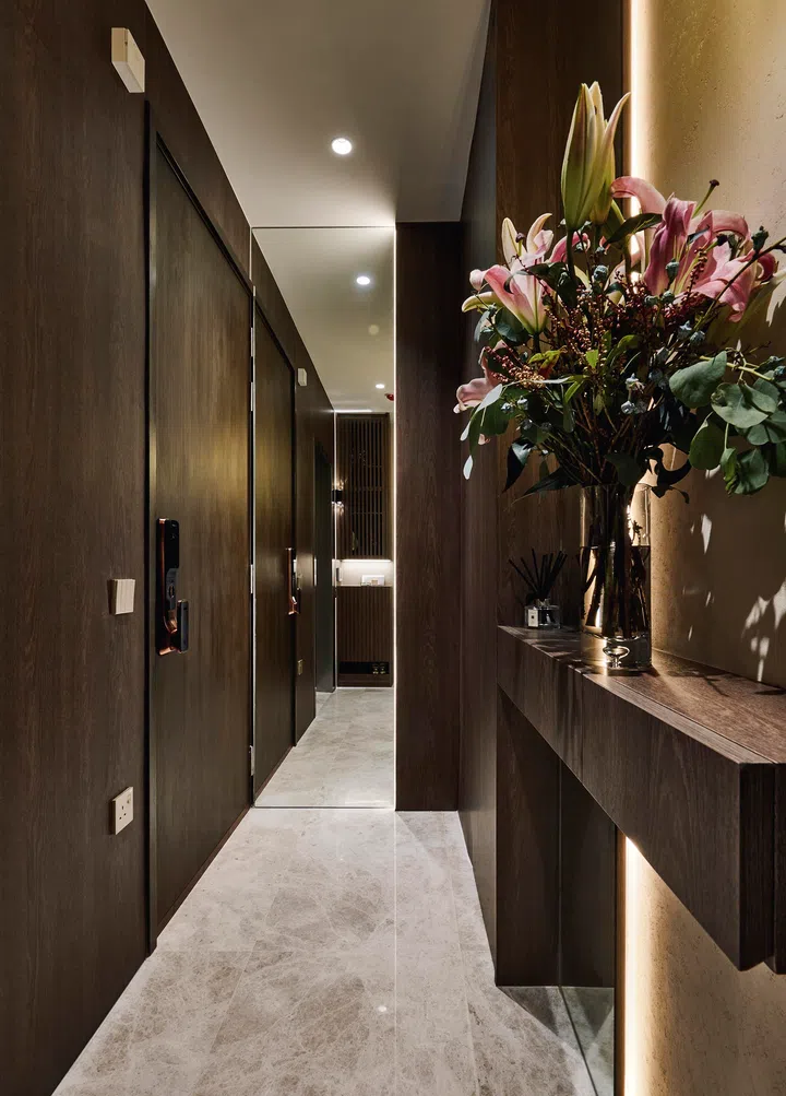 Dark-toned carpentry and a travertine backdrop set a calm, grounding tone, with fresh flowers adding a welcoming pop of colour.