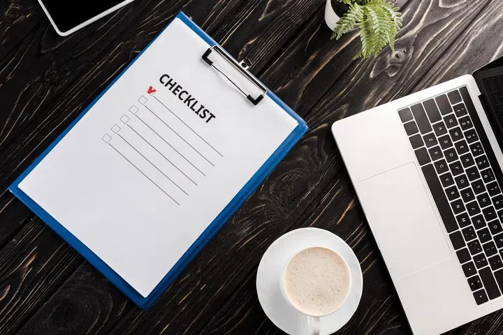 top view of clipboard with checklist letters near laptop, plant and cup of coffee on table, e-commerce concept