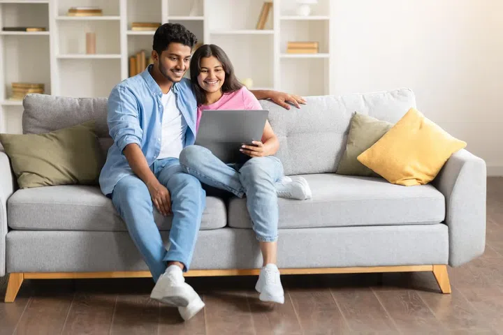 Happy Indian couple on sofa, using laptop computer together, free space. Photo 123RF