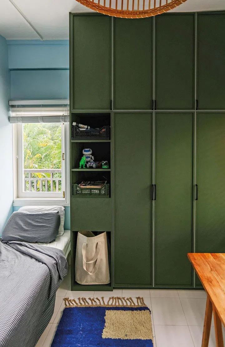 A single bed under the window, with green cabinets beside