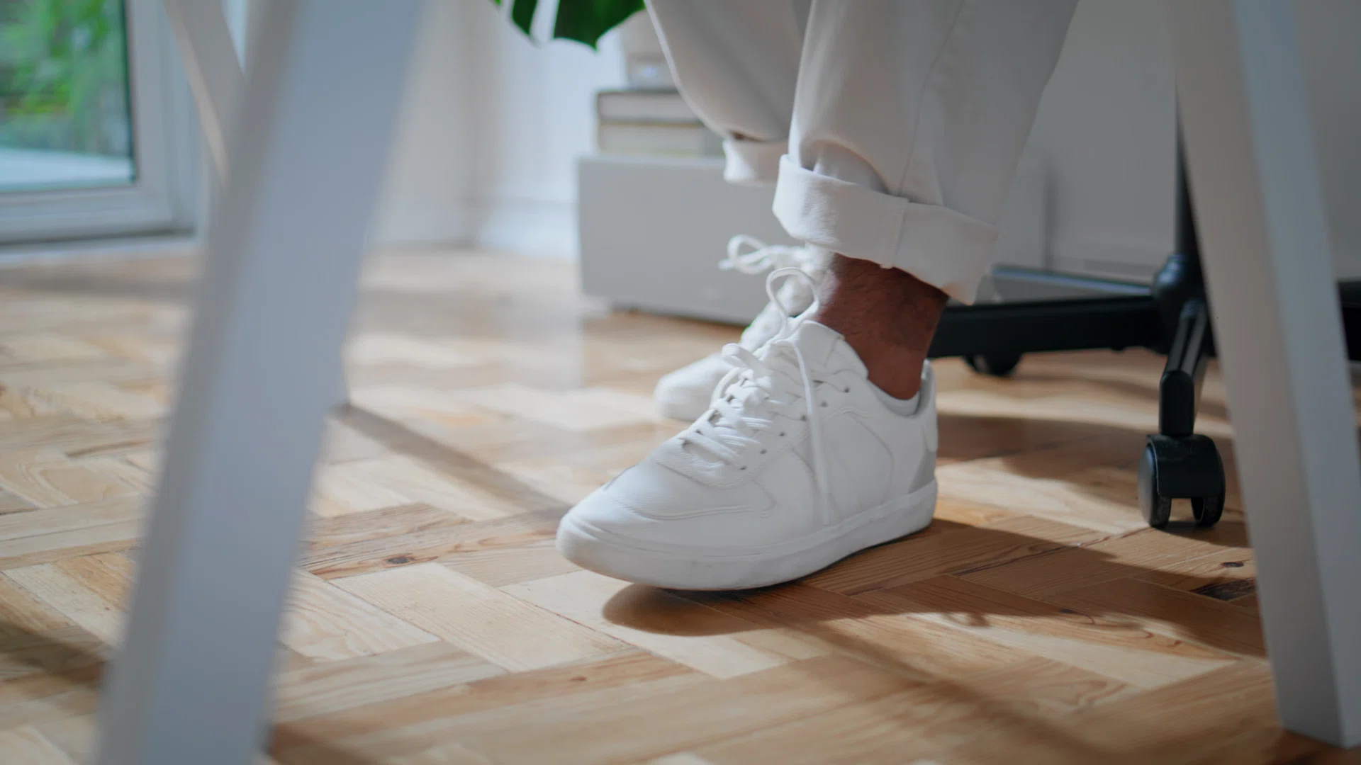 White man shoes sitting chair at home closeup. Contemporary african american freelancer legs moving under desk in room. Anonymous guy in modern sneakers working table alone at home remote workplace