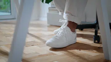 White man shoes sitting chair at home closeup. Contemporary african american freelancer legs moving under desk in room. Anonymous guy in modern sneakers working table alone at home remote workplace
