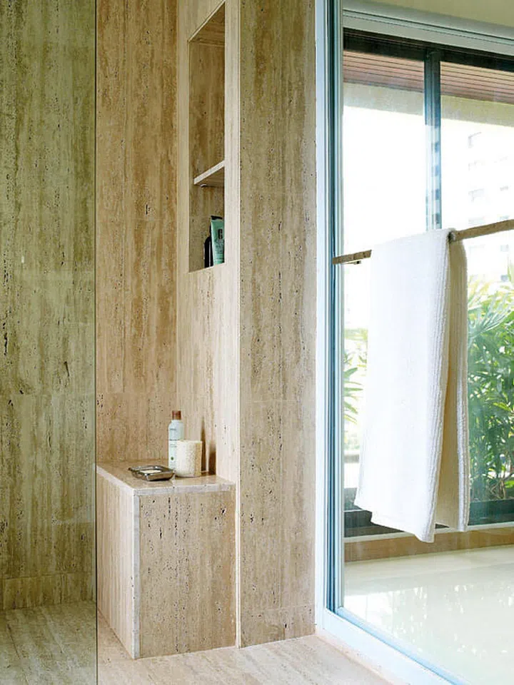 For a sense of opulence, luxurious materials like marble and glass were used in the bathroom. Travertine marble adds a classic air to the small shower, making it feel like a roman bath. The pitted marble was smoothed out for the floors.